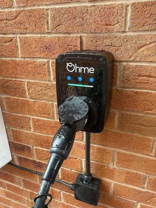 Ohme EV charger plugged in on a brick wall